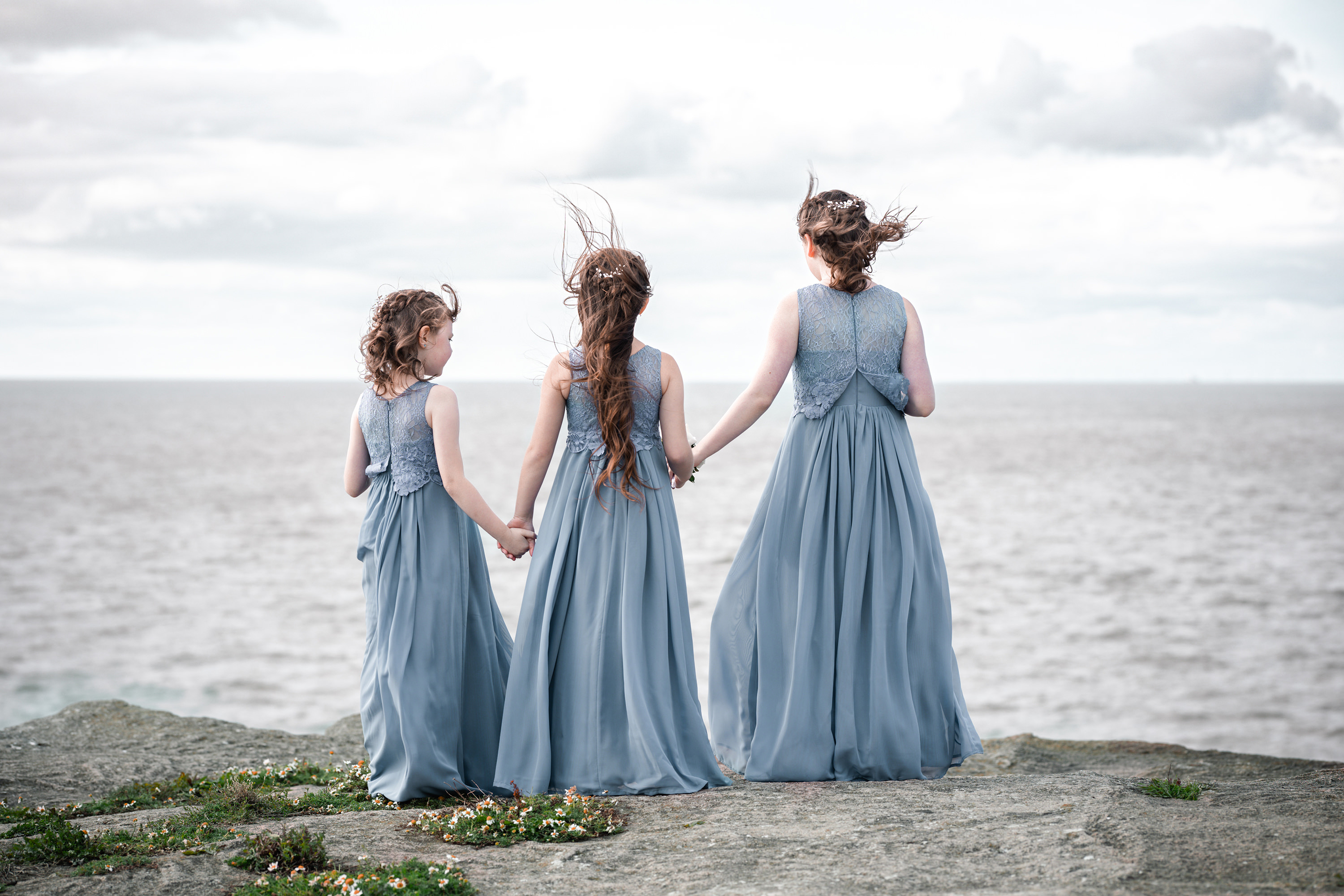 The flower girls hold hands as they look out to sea 