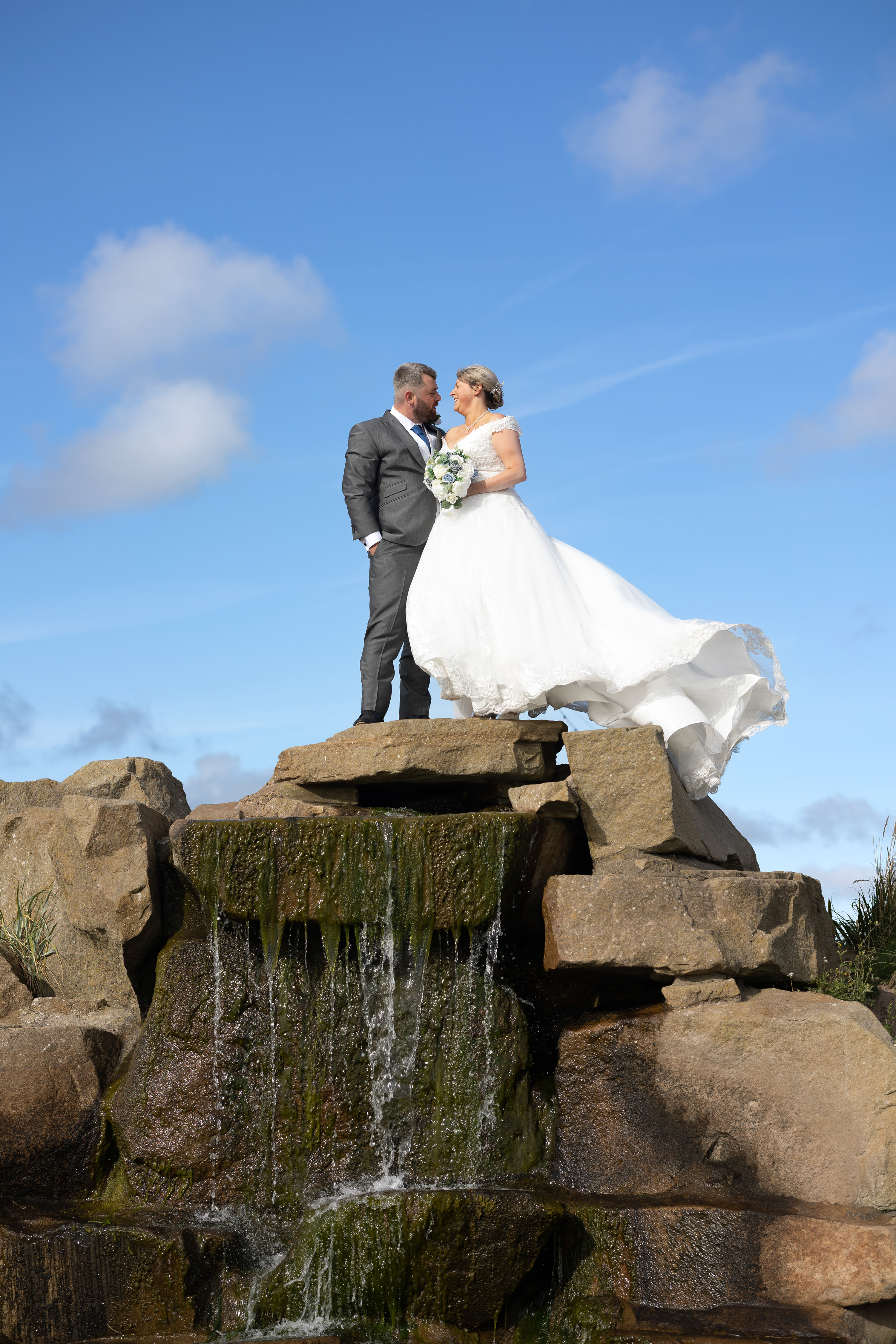The bride and groom pose for a wedding photo on top of the waterfall 