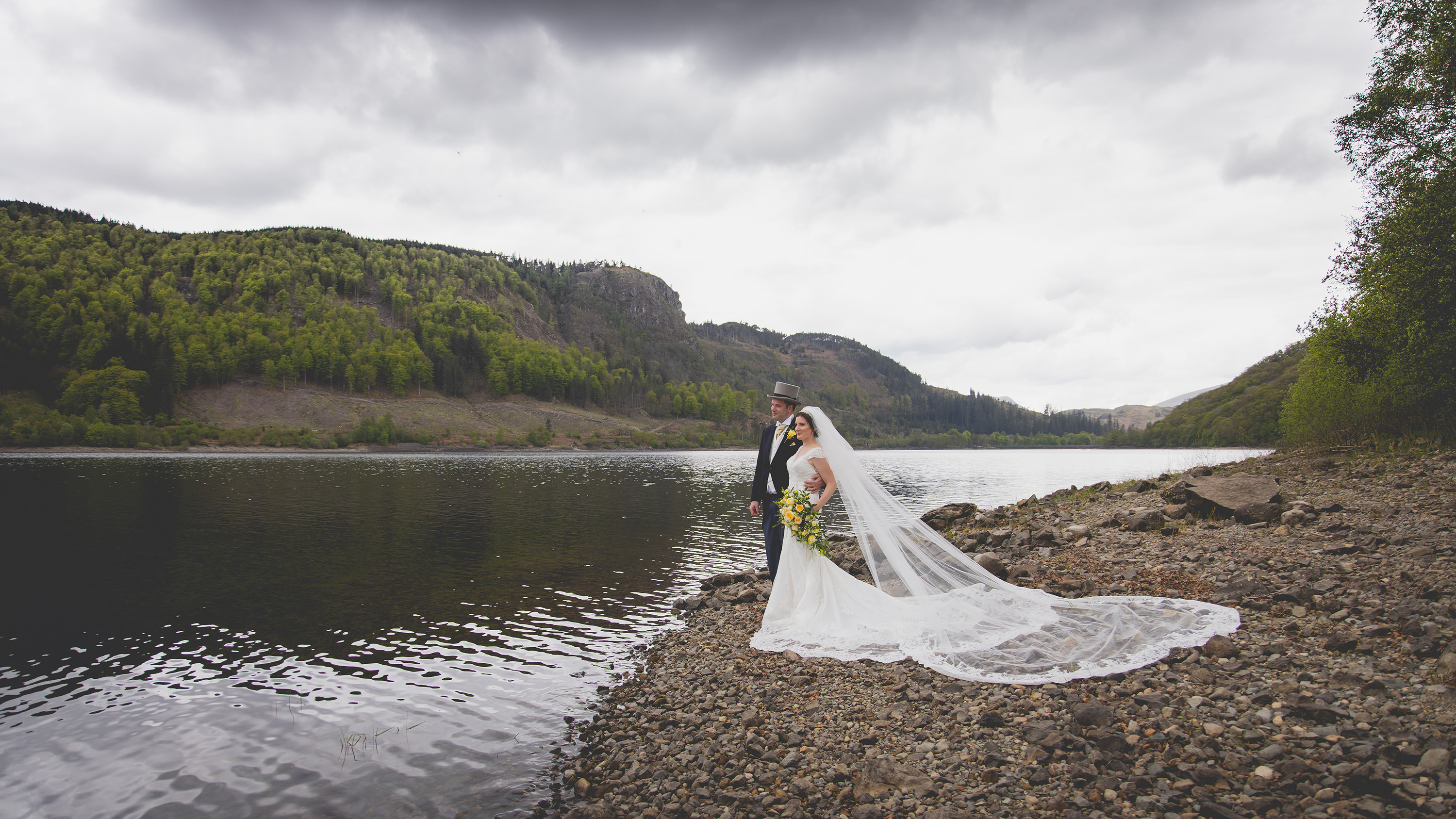 The bride and groom pose for a photo on the edge of Lake Thirlmere