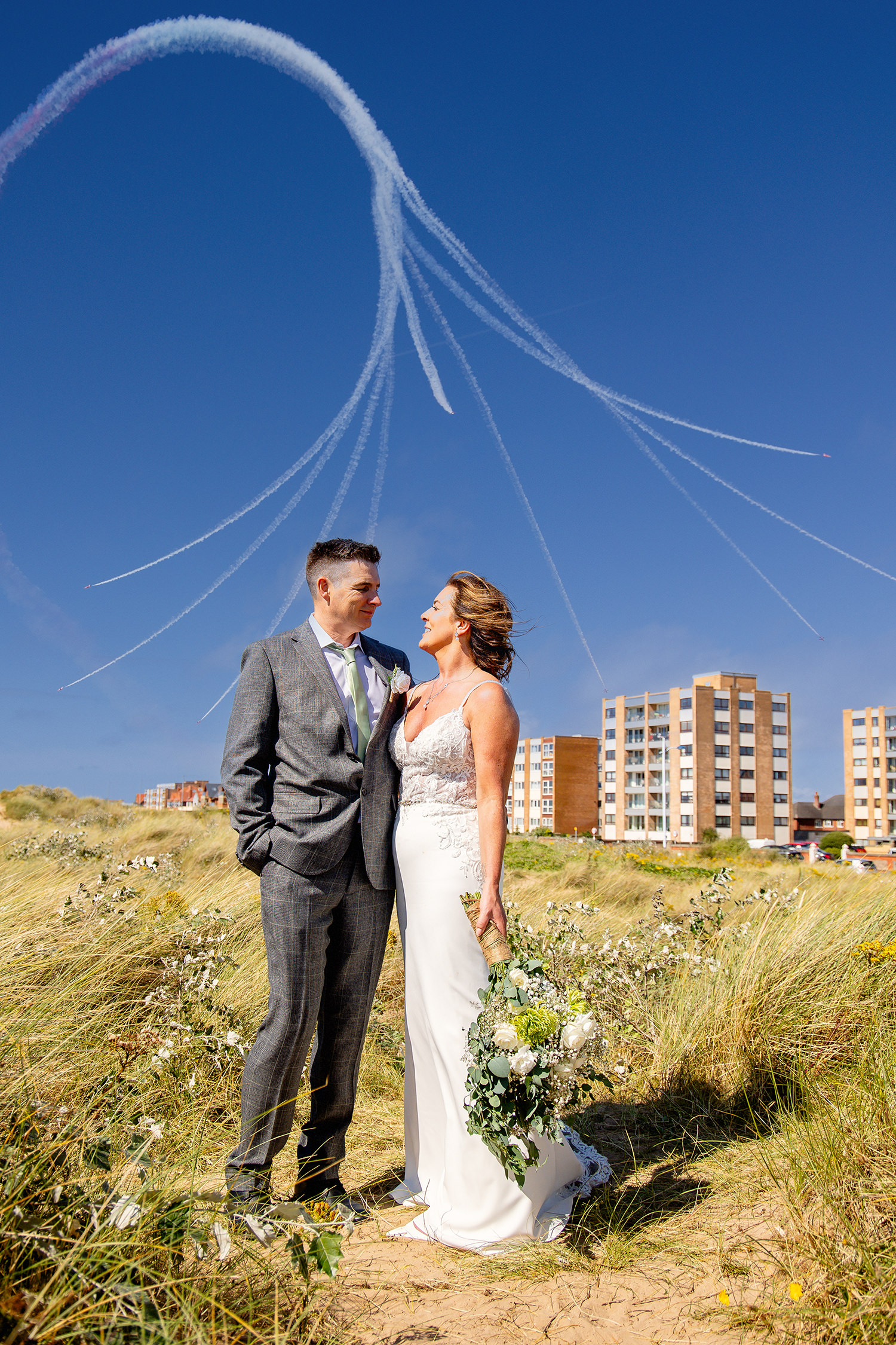 The bride and groom standing on the sand dunes with the Red Arrows behind them