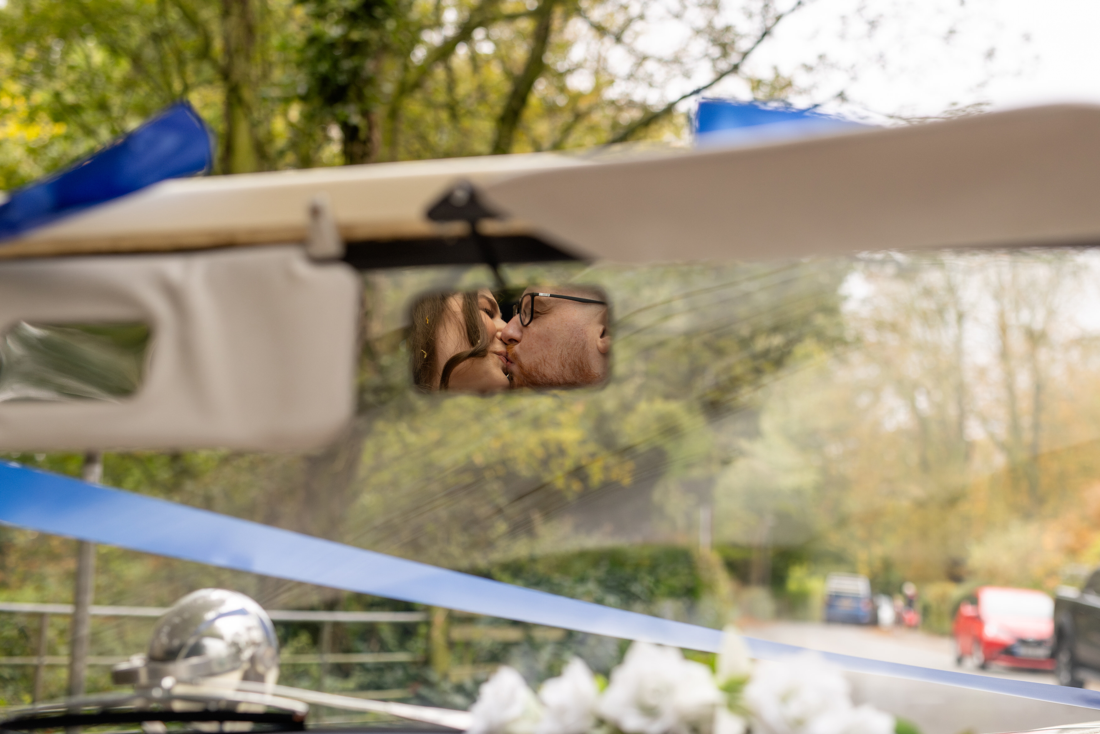 A reflection of the bride and groom kissing in the rear view mirror 